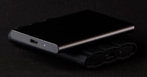 Two sleek external hard drives, one stacked on top of the other, are shown on a black surface. Both drives are black with USB-C ports visible, and the top drive has a small indicator light.