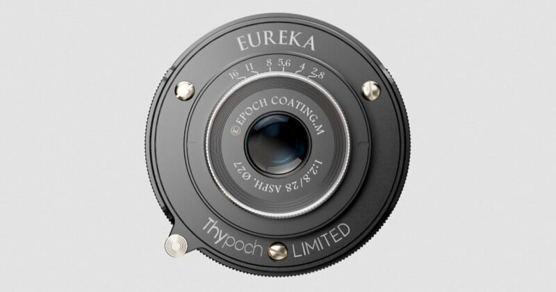 A close-up, top-down view of a black camera lens labeled "EUREKA" with aperture markings, metallic screws, and text including "Thypoch LIMITED" and "Epoch Coating 1:2/28 ASPH Ø37.
