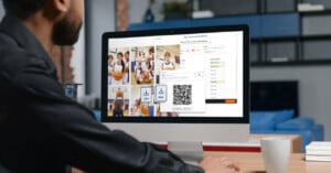 A person sits at a desk using a computer displaying images of a youth basketball team, a QR code, and options to download data as CSV or PDF files. A coffee cup is on the desk.