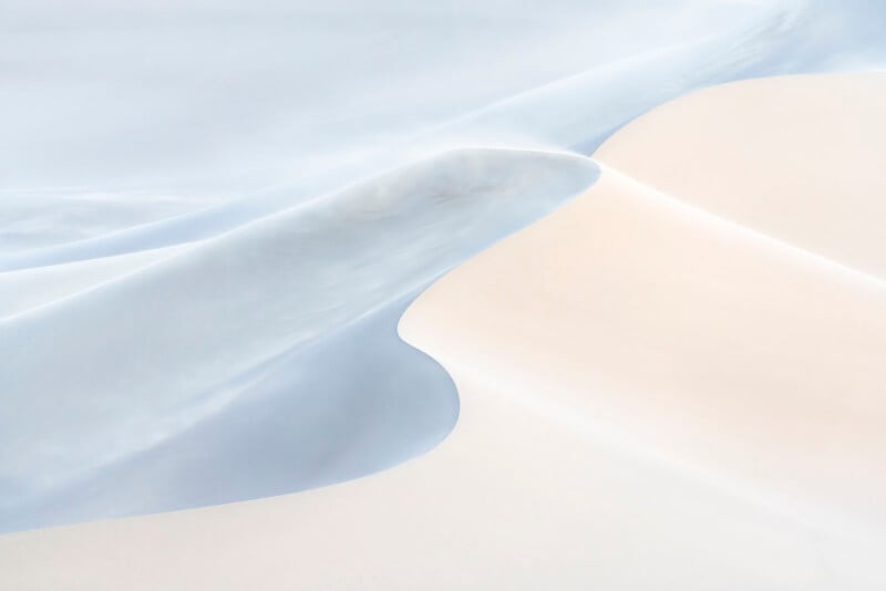 Un paisaje suave y abstracto de dunas pálidas, con curvas suaves y fluidas en blanco y azul claro, crea una escena tranquila y minimalista.