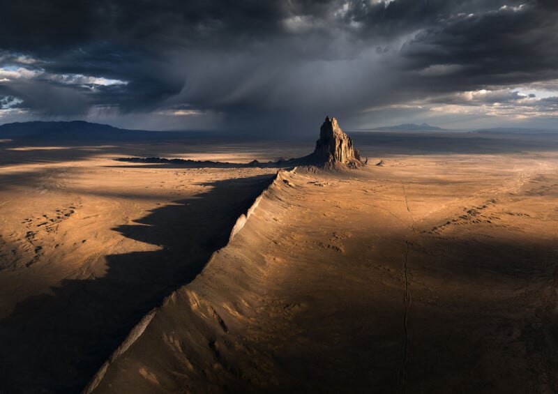 Enormes rocas se elevan en el vasto desierto bajo un cielo sombrío, y el sol proyecta largas sombras sobre la tierra árida.