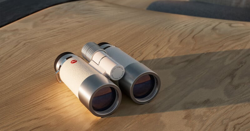 A pair of modern white binoculars with metallic accents rests on a light wood surface, illuminated by soft natural light.