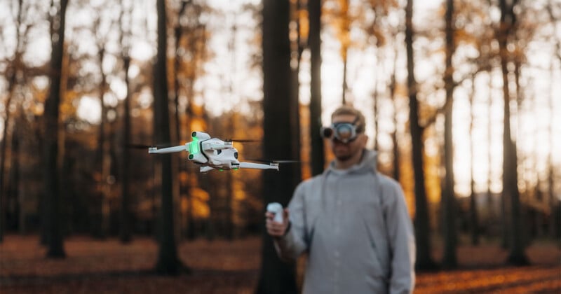 Un hombre con gafas FPV opera un dron a control remoto en un bosque con árboles altos y exuberante follaje otoñal.