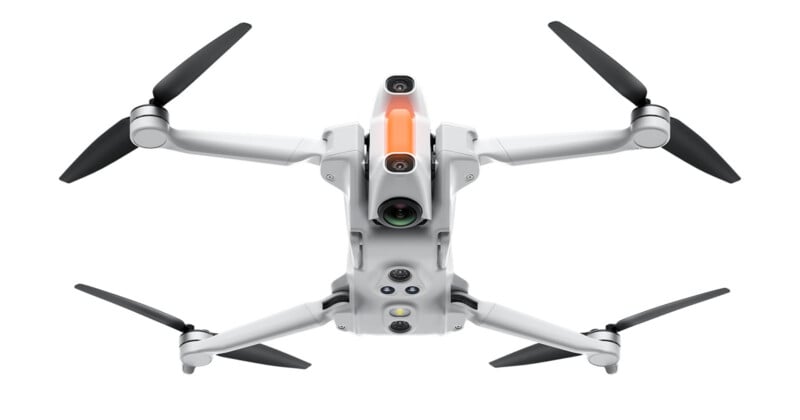 Un dron cuadricóptero blanco con cuatro hélices negras, múltiples cámaras y sensores, visto desde abajo, aislado sobre fondo blanco.