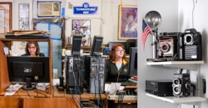 Two women sit at cluttered desks with computers in an office; to the right, shelves display vintage cameras, an old radio, and an American flag. A "Donnaruma Way" sign hangs on the wall behind them.
