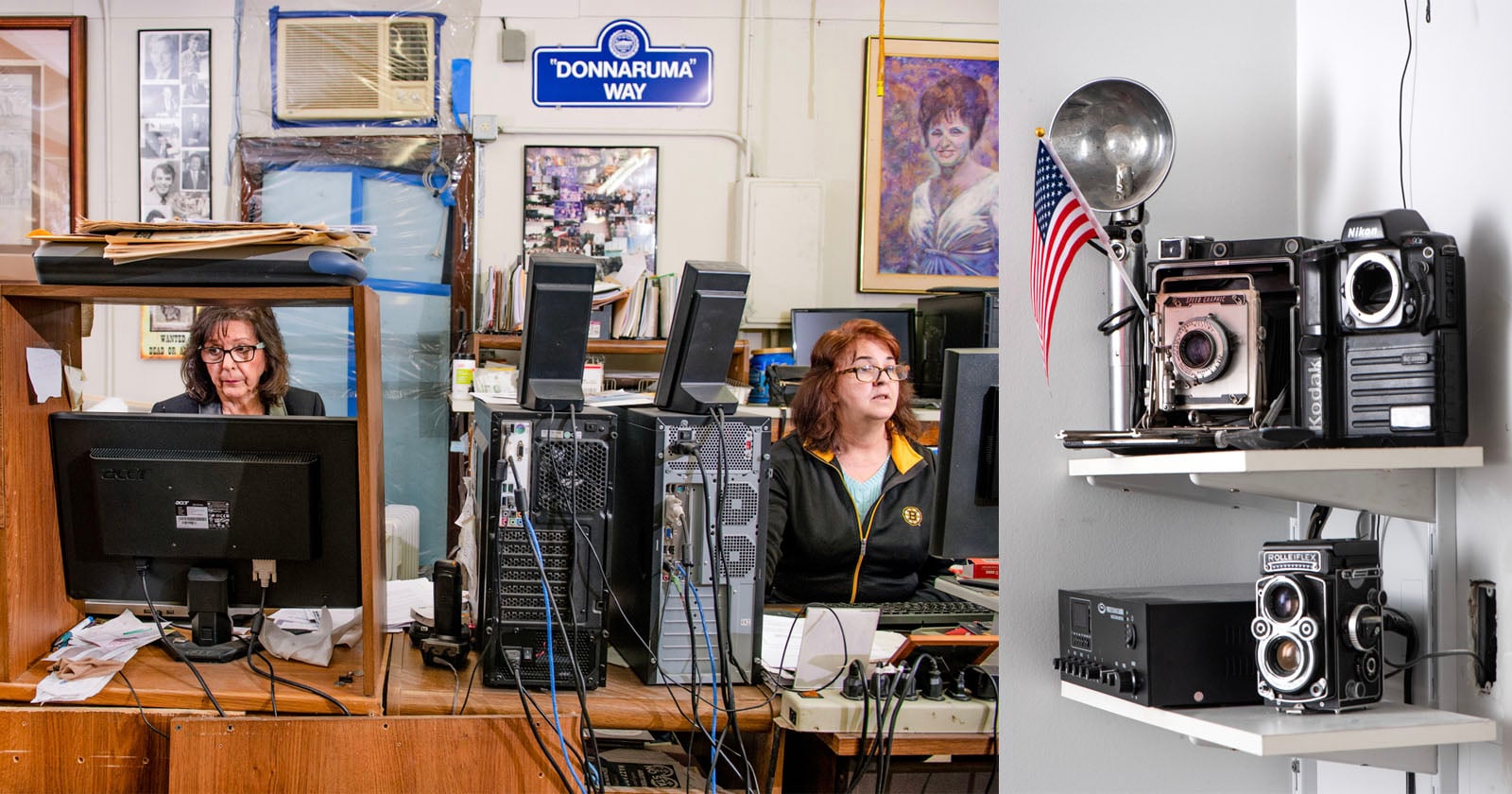Two women sit at cluttered desks with computers in an office; to the right, shelves display vintage cameras, an old radio, and an American flag. A "Donnaruma Way" sign hangs on the wall behind them.