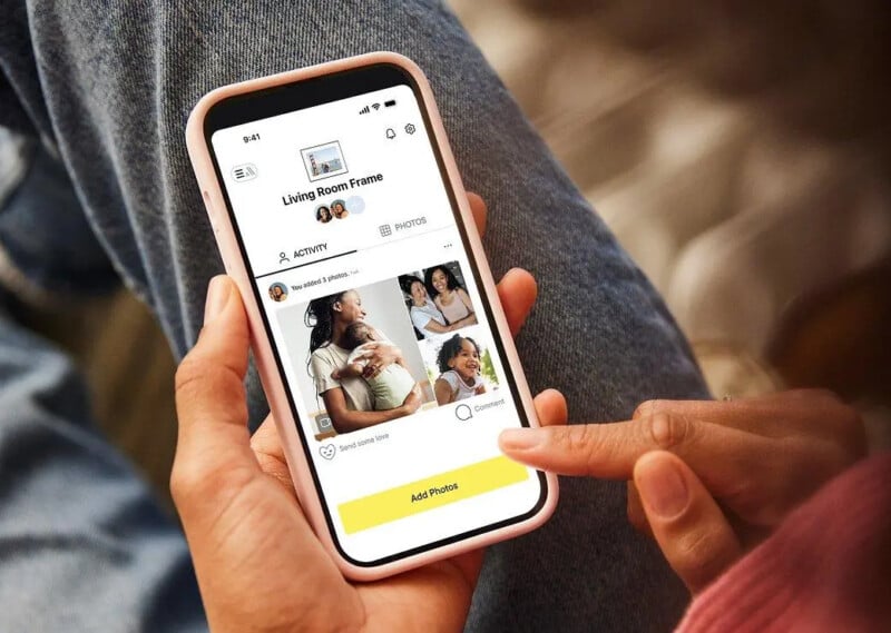 Una persona sostiene un teléfono inteligente que muestra una aplicación para compartir fotografías con imágenes de mujeres y niños. Pantalla que muestra opciones de actividades, fotos y comentarios en amarillo "agregar foto" El botón está en la parte inferior.