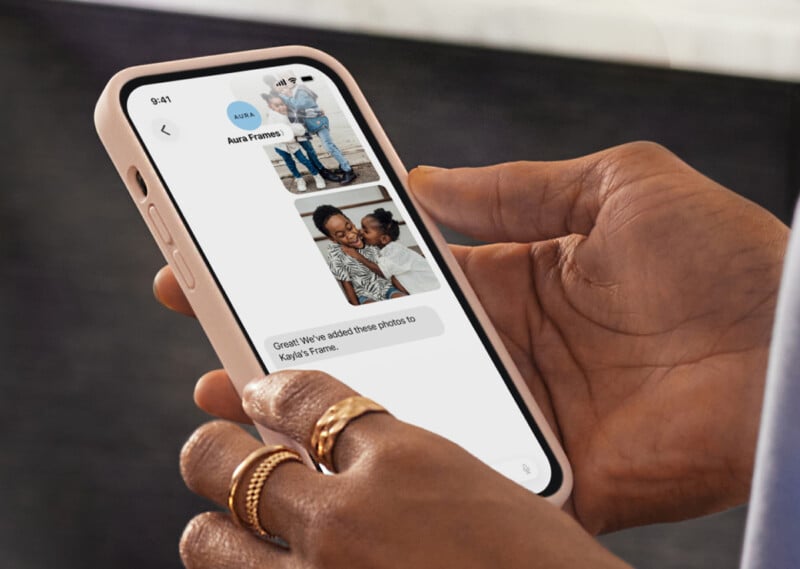 Una persona que sostiene un teléfono inteligente ve una aplicación de mensajería que muestra una foto de dos niños y un adulto con un niño, acompañada de un mensaje: "¡Excelente! Hemos agregado estas fotos al marco de fotos de Kayla.