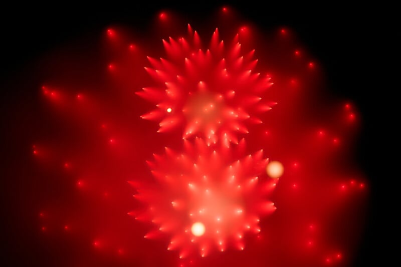 Red fireworks burst in the night sky, creating two bright, spiky circular patterns with glowing points of light radiating outward against a black background.