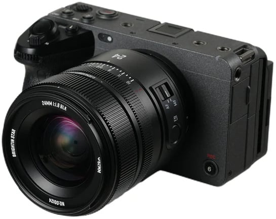 A black digital mirrorless camera with a large detachable 24mm lens, showing various buttons, dials, and markings on the camera body and lens barrel.