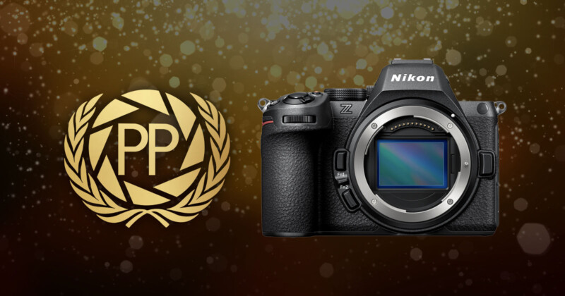 A Nikon Z camera body is displayed next to a gold laurel wreath emblem with the letters "PP" on a dark, sparkling background.