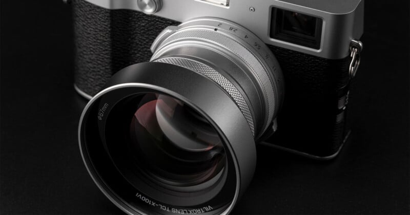 Primer plano de una cámara digital plateada y negra con lente grande colocada sobre una superficie oscura. La atención se centra en la lente de la cámara y el cuerpo texturizado, resaltando su detalle y diseño.