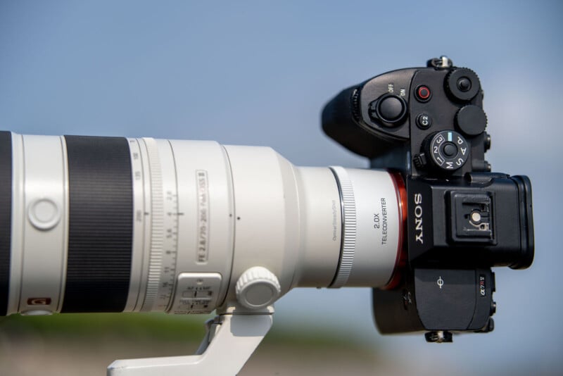 Primer plano de la cámara Sony con un gran teleobjetivo blanco centrado en el fondo del cielo azul. Los controles de la cámara y los detalles de la lente son claramente visibles.