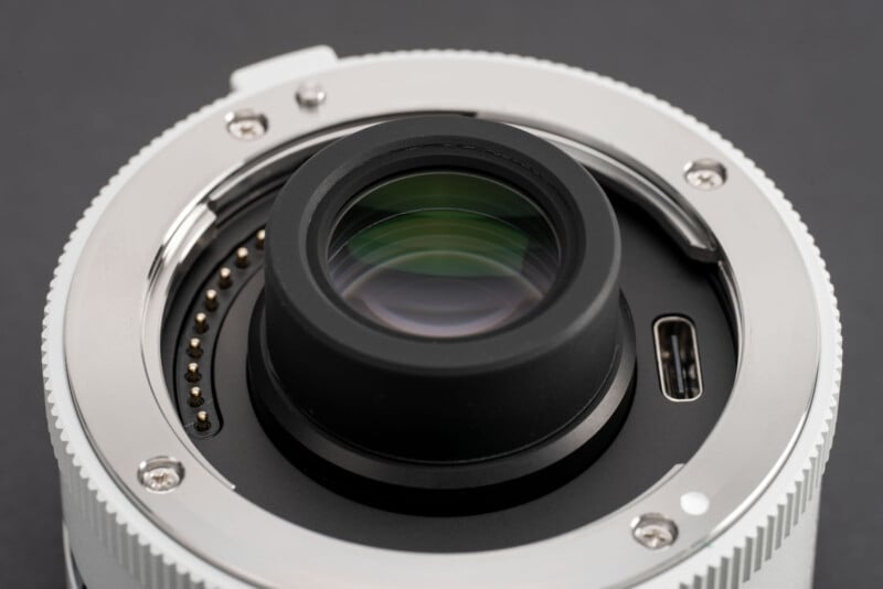 Primer plano de la montura de la lente de la cámara con contactos electrónicos y puerto USB-C, que muestra el elemento de vidrio trasero y la montura metálica sobre un fondo oscuro.