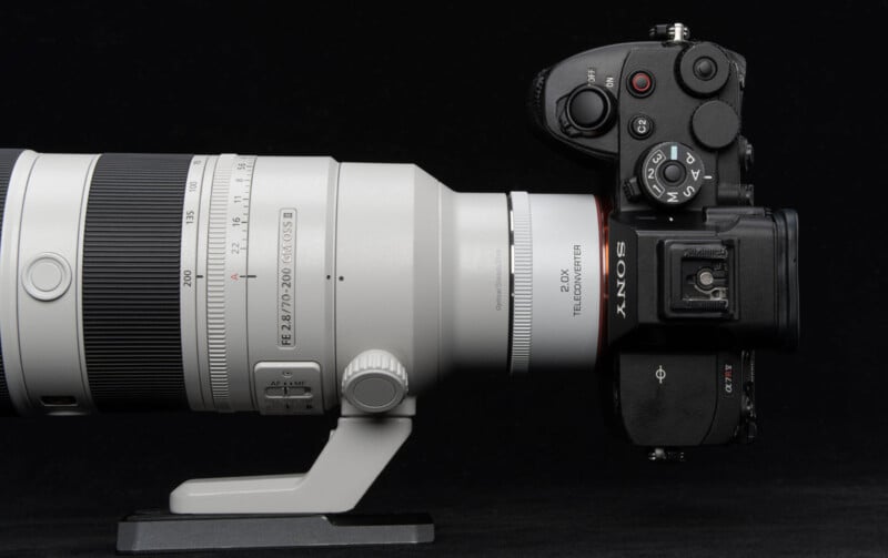 Una cámara sin espejo de Sony con un gran teleobjetivo con zoom blanco montado sobre un anillo de trípode negro sobre un fondo negro.