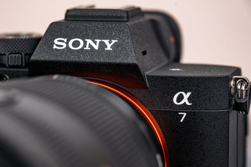 Close-up of a black Sony Alpha 7 camera showing the "SONY" logo and "α7" model label, with part of the camera lens visible in the foreground.