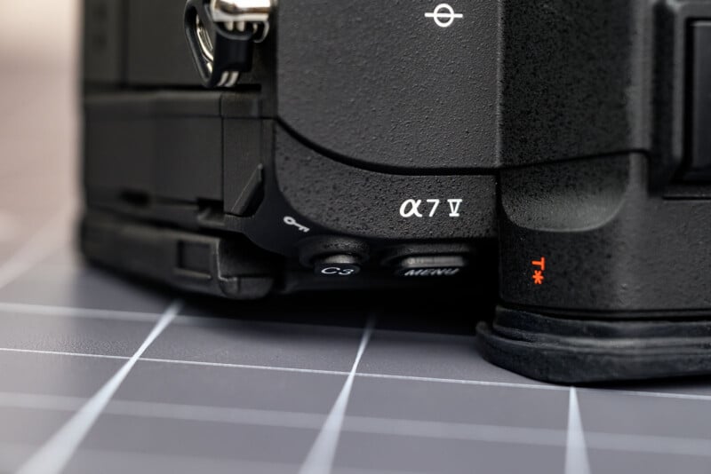 Close-up of a Sony Alpha 7 IV camera body, showing the model label "α7 IV," control buttons, and part of the camera grip, placed on a gray grid-patterned surface.
