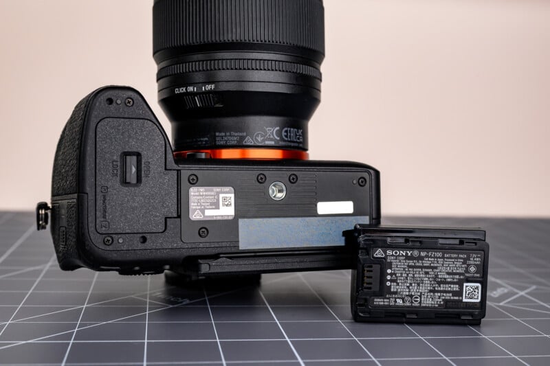 A close-up of the bottom of a Sony camera body placed on a table next to a detached Sony NP-FZ100 battery, with details and labels visible on both items.