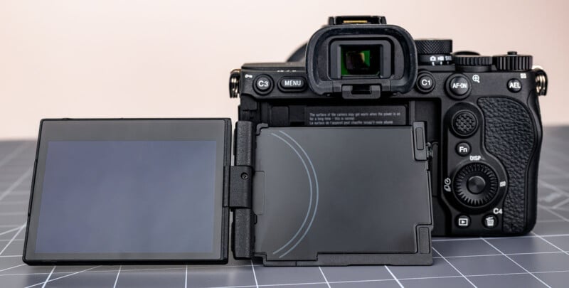 A digital camera viewed from the back, showing its open, articulated LCD screen extended to the left side, displaying the camera’s buttons, dials, and electronic viewfinder.