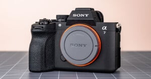 A Sony Alpha 7 mirrorless digital camera body with an E-mount cap, shown on a grid-patterned surface against a plain, light-colored background.