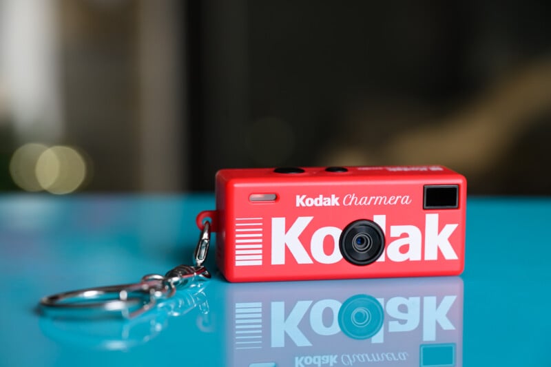 Llavero pequeño de cámara Kodak roja con etiqueta "Cámara Kodak" Situado sobre una superficie azul brillante con un fondo borroso.