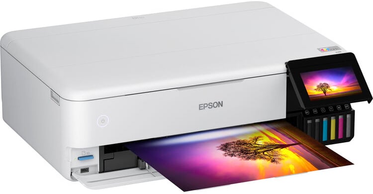 Una impresora Epson blanca imprime una fotografía vibrante y colorida de un árbol al atardecer. La impresora tiene una pantalla táctil con tanques de tinta cian, magenta, amarillo y negro visibles en el lado derecho.
