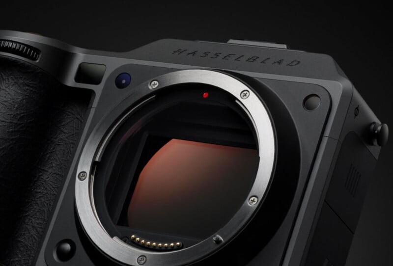 Close-up of a Hasselblad camera body, focusing on the lens mount and sensor, with the brand name "Hasselblad" visible on the top edge. The surface is matte black with textured grips.