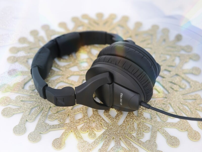 Un par de audífonos supraaurales Sennheiser negros se encuentran sobre un mantel individual dorado brillante con forma de copo de nieve, con una iluminación suave y un fondo borroso.