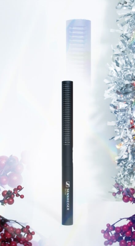 Un micrófono Sennheiser negro se encuentra en posición vertical en el centro, rodeado de decoraciones festivas, bayas rojas a la izquierda y oropel plateado a la derecha, sobre un fondo brillante y suave.