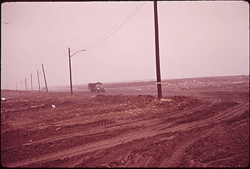 Un camino de tierra con profundas huellas de neumáticos atraviesa el paisaje árido. La carretera está bordeada de postes telefónicos y a lo lejos se ve un camión volquete. El cielo estaba nublado y el suelo estaba cubierto de escombros.