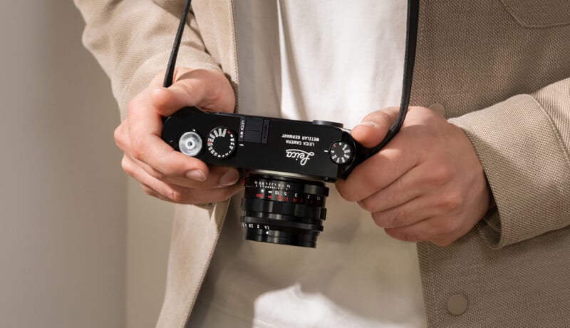 Un hombre sostiene una cámara cinematográfica Leica negra con ambas manos y viste una chaqueta beige claro. El dial y la lente de la cámara son claramente visibles.