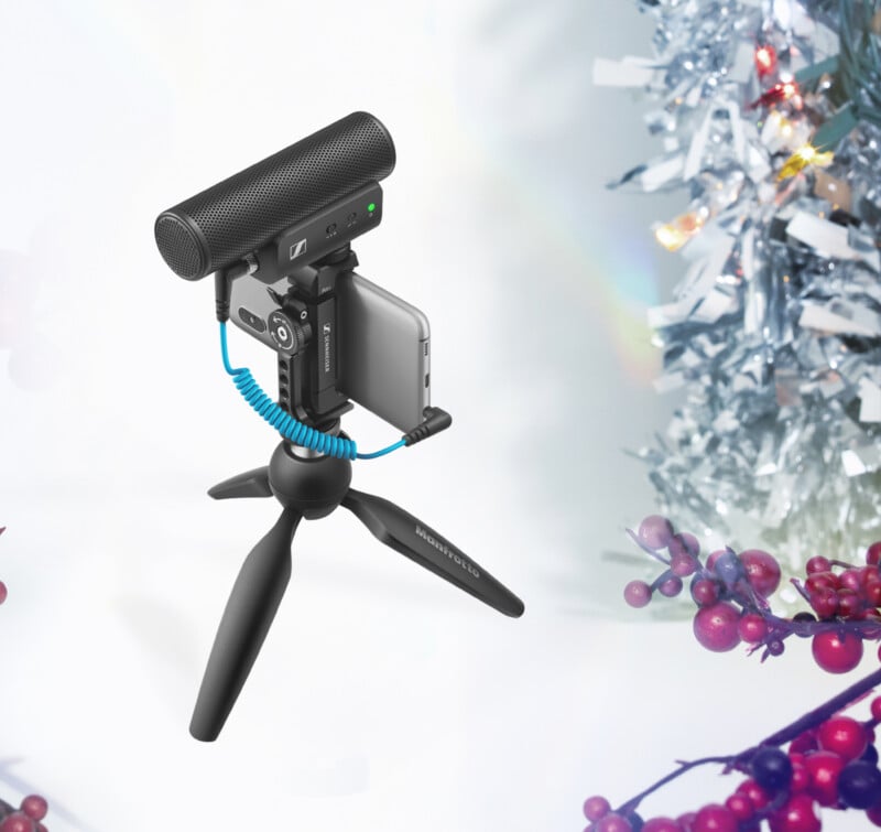 Una cámara compacta con un micrófono externo montado en un pequeño trípode. Ramas de bayas y oropel plateado decoran toda la escena, creando un ambiente festivo.