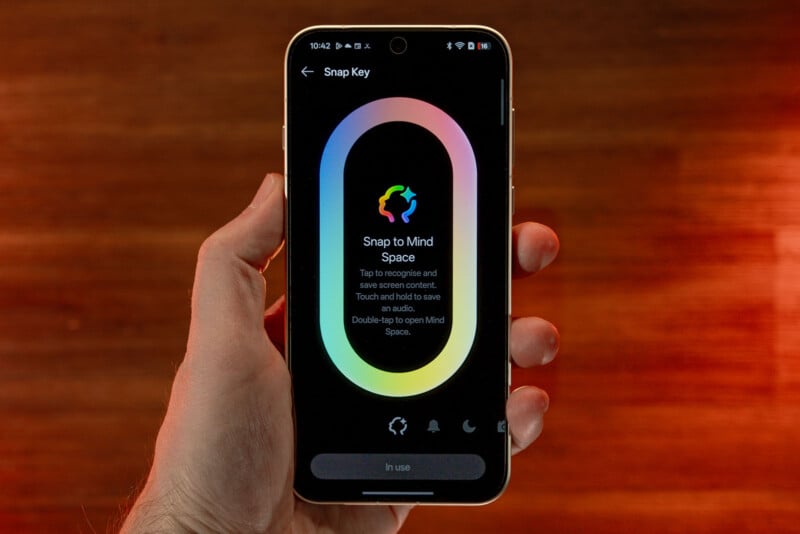 A hand holding a smartphone displaying an app called "Snap Key." The app screen features a colorful oval with instructions to record and save audio by tapping, and to open "Mind Space" by double-tapping.