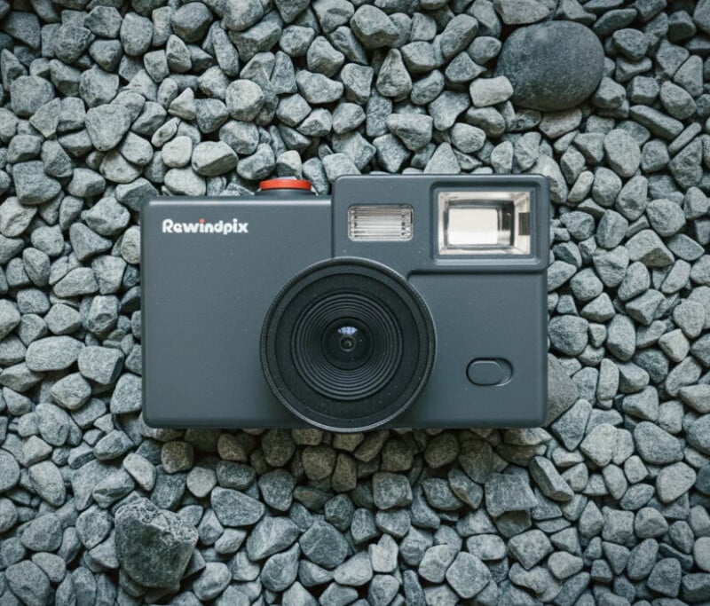 Vista desde arriba, una cámara instantánea Rewindpix negra se encuentra sobre una superficie cubierta de guijarros grises.