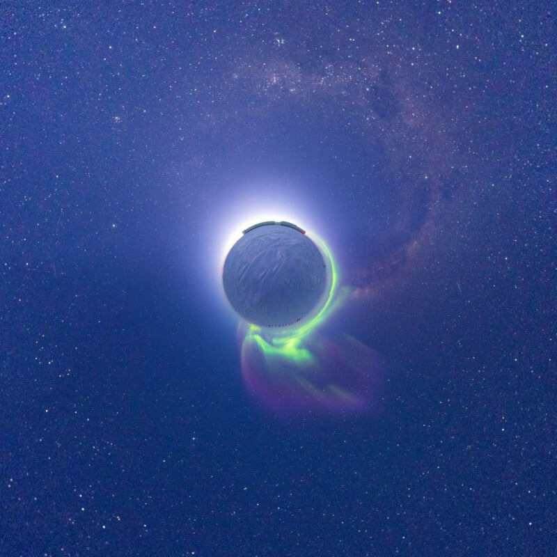 A glowing planet-like sphere with green and purple auroras is surrounded by a halo of light and stars against a dark, star-filled sky. The image has a surreal, cosmic atmosphere.