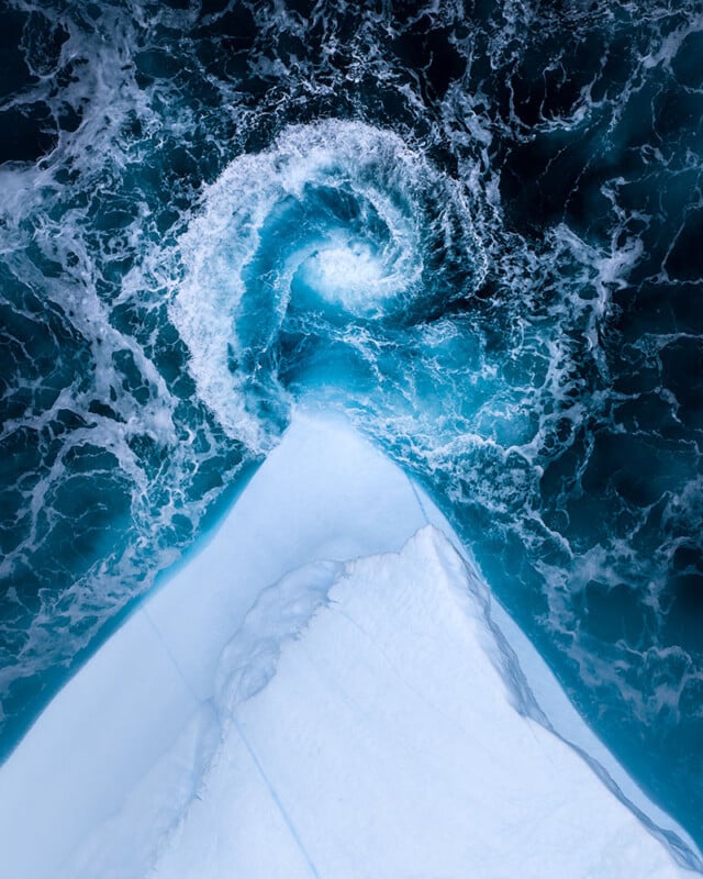 A vista de pájaro del iceberg, el agua turquesa gira en espiral alrededor de la cima del iceberg, formando espectaculares olas espumosas en el mar azul profundo.