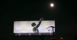 A billboard at night shows a black-and-white image of a basketball player shooting, with the words "STEPHEN CURRY" and "SHOT READY." A full moon glows above the billboard in the dark sky.