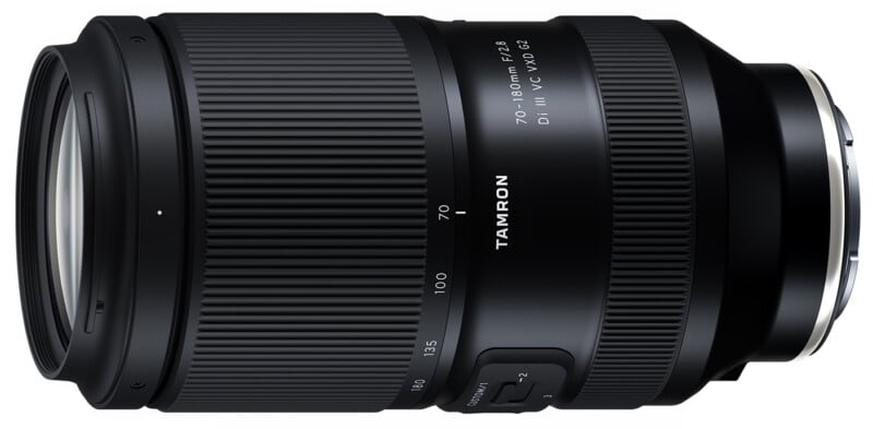 Lente de zoom Tamron 70-180 mm f/2.8 Di III VC VXD G2 negra, mostrada horizontalmente con anillos de enfoque y zoom visibles, marcas de lentes y varios interruptores en el lateral.