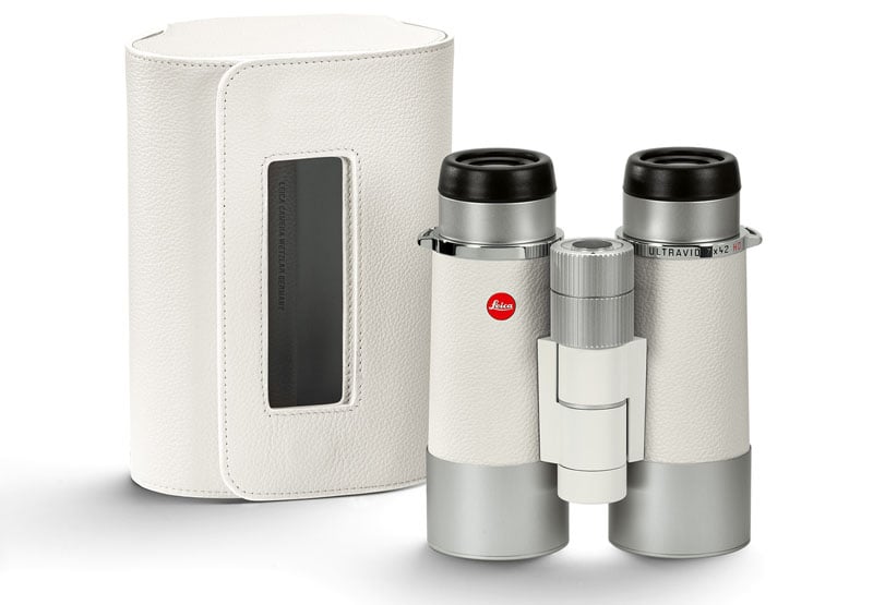 A pair of sleek, white Leica binoculars with silver accents is displayed next to a matching white protective case with a clear vertical window.