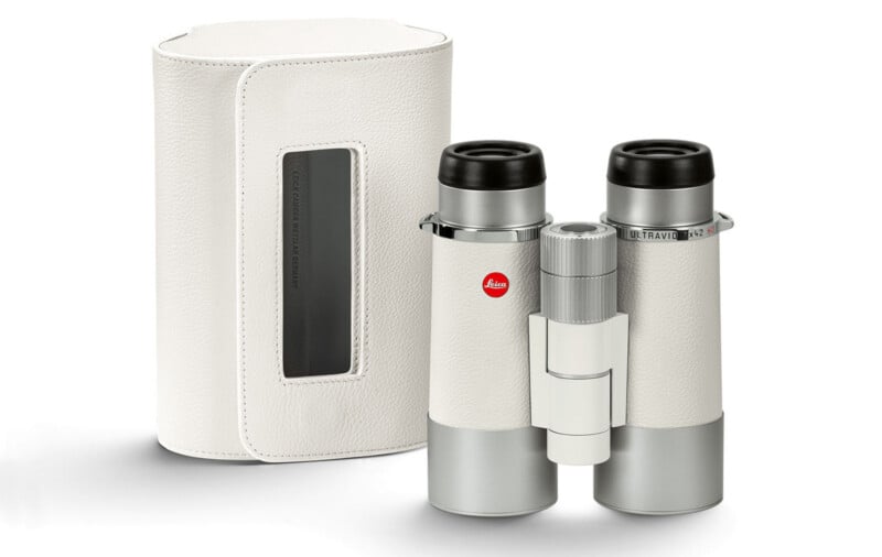 A pair of white and silver binoculars with a red Leica logo, shown next to a matching white carrying case with a transparent window and black detailing.