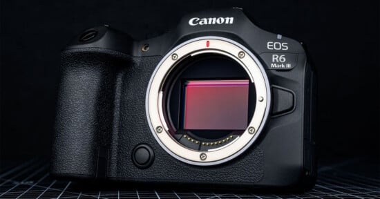 A Canon EOS R6 Mark III mirrorless camera body is shown without a lens, revealing its image sensor, on a dark, grid-patterned surface.
