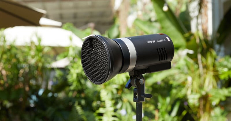 Luz estroboscópica Godox AD300Pro Studio con difusor de malla adjunto, montada sobre un soporte de luz, colocada al aire libre con vegetación y follaje borroso en el fondo.