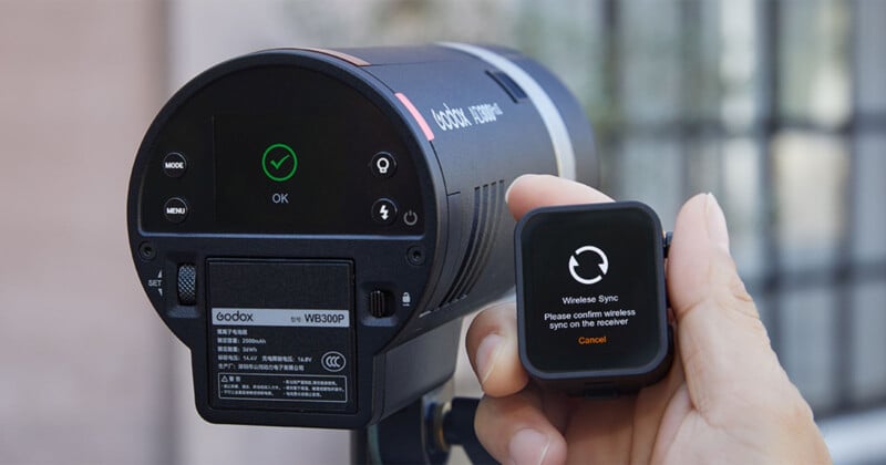Una mano sosteniendo el disparador inalámbrico Godox AD600Pro cerca del flash que muestra un mensaje de confirmación de sincronización con una marca de verificación verde y "DE ACUERDO" en sus pantallas digitales.