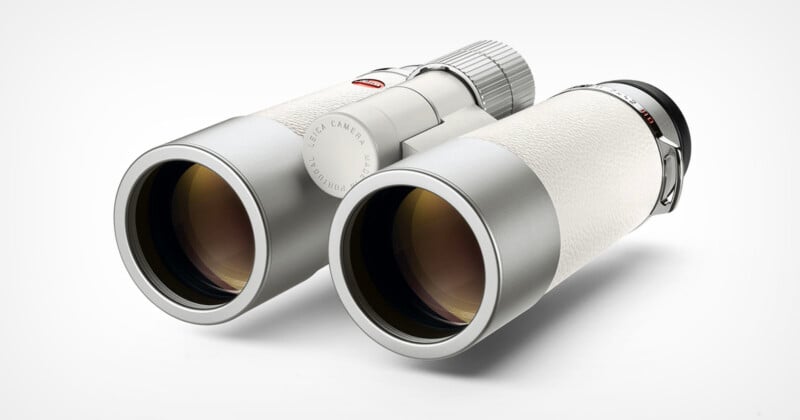 A pair of sleek, modern white binoculars with metallic accents is shown on a light background, viewed from an angle that highlights the lenses and textured surface.