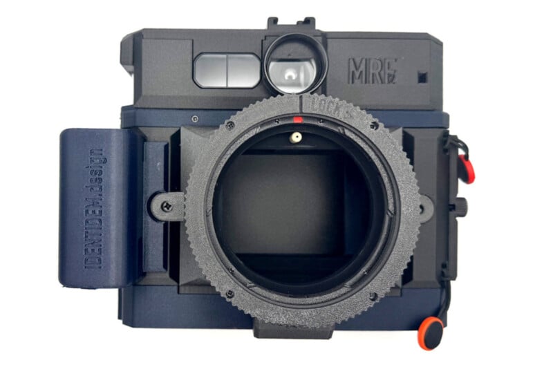 A close-up view of a black camera body with no lens attached, revealing the lens mount. The camera has a viewfinder, a grip labeled "NEW DEM-8 35/37," and various buttons and dials.
