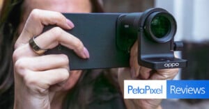 Close-up of a person holding an Oppo smartphone with an attached camera lens, preparing to take a photo. The Petapixel Reviews logo appears in the bottom right corner.