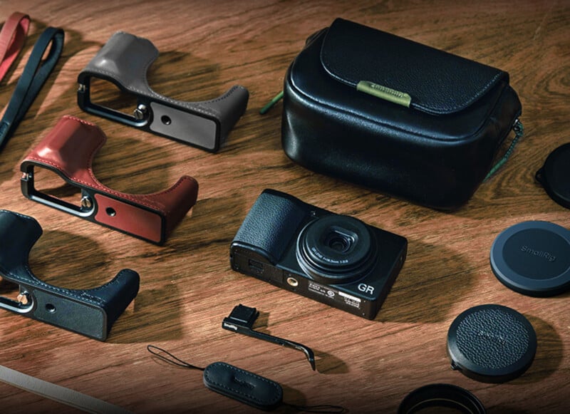 Pequeñas cámaras, empuñaduras de cuero de diferentes colores, estuches negros, tapas de lentes y pequeños accesorios para cámaras están cuidadosamente dispuestos sobre una superficie de madera.