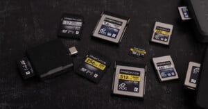 Several ProGrade memory cards of different sizes and capacities are arranged on a black surface alongside a black USB card reader. The cards display various speed and storage labels in yellow and gray.