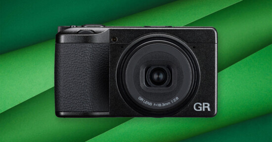 A compact black digital camera with a prominent GR lens is centered on a background of overlapping green paper strips.