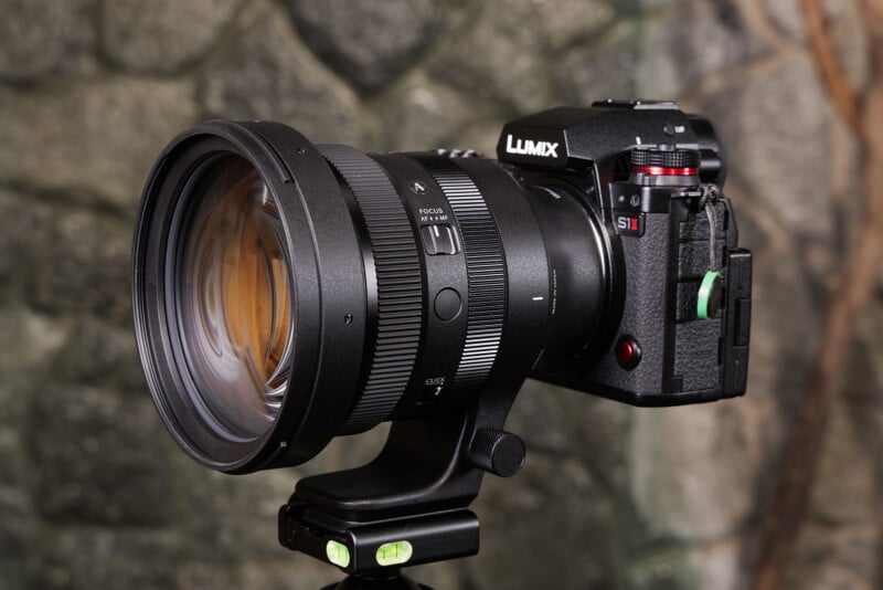 Una cámara Panasonic Lumix S1 con su gran teleobjetivo montado sobre un trípode sobre un fondo de piedra texturizada.